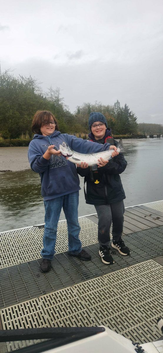 Two young anglers standing on a dock together holding a coho salmon